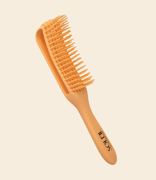 Yellow Soleil brush with long bristles for detangling hair against a beige background