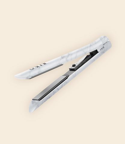 Soleil flat iron with marble pattern, black ceramic plates, and on/off button. Set against a beige background